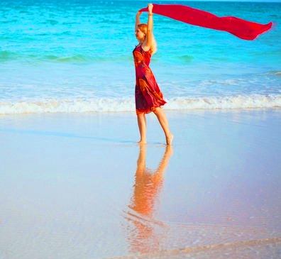 Woman in Bright Red Sarong and Scarf Walking along the Beach